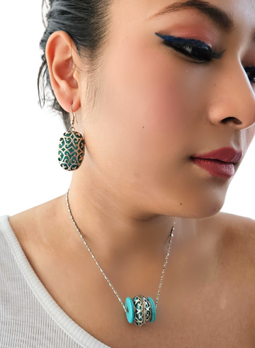 A close-up image of a woman wearing a turquoise and silver pendant necklace with a barrel design.