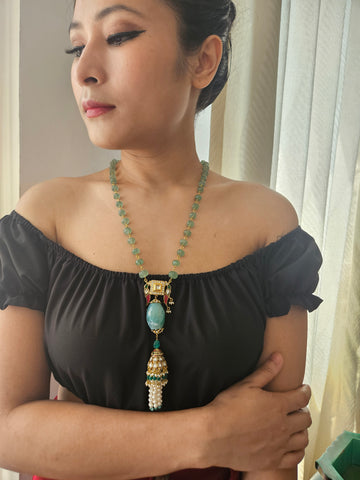 A person wearing a black off-shoulder top showcasing a gold-linked aventurine necklace with a traditional kundan bird pendant and pearl tassels.