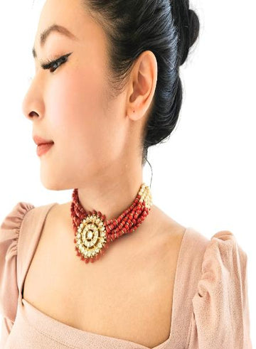 A woman wearing a multi-string coral kundan choker with a circular kundan piece.