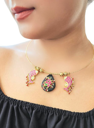 A woman wearing a gold hasli necklace with a black onyx drop pendant and small fish-shaped charms.