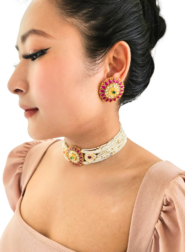 A person wearing a multi-string pearl choker necklace with a dramatic circular kundan and ruby piece.