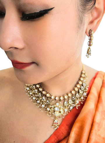 Close-up of a woman wearing a gold necklace and earrings with an orange garment.