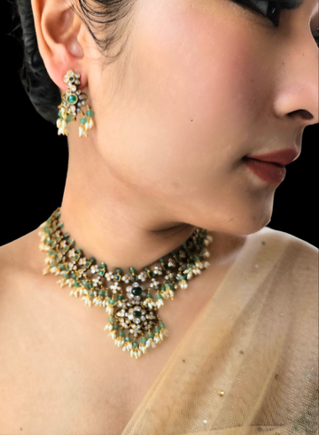 A person wearing a green onyx polki necklace with rice pearl accents and matching earrings.