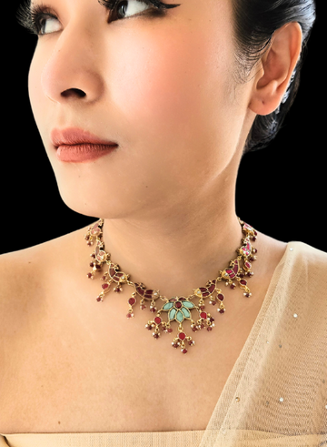 A person wearing a kundan and ruby fish necklace with a turquoise flower centerpiece.
