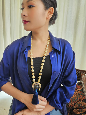 A person wearing a blue shirt and a black topaz necklace with pearl-like beads and a sapphire pendant.