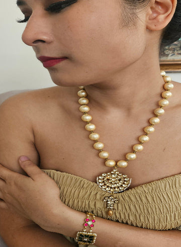A person wearing a traditional beige dress with a gold and multicolor beaded necklace and matching bracelet.