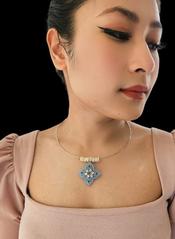 A close-up image of a woman wearing a delicate blue agate pendant necklace with a thin gold chain and pearl accents.