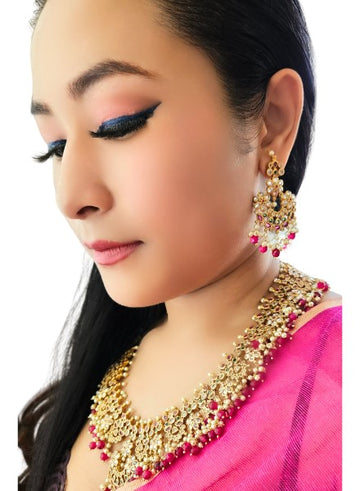 A person wearing a traditional gold, pearl, and ruby necklace with matching earrings.