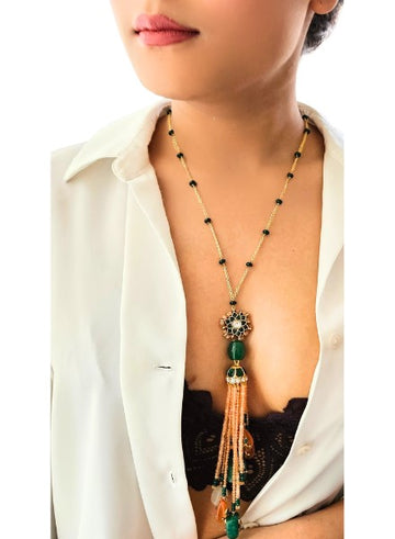 A person wearing a white shirt with a light orange agate and green jade tassel necklace.
