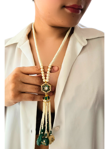 A person wearing a white shirt showcases a stunning pearl necklace with green Kundan accents and pearl tassels.