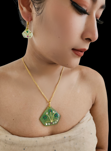 A person wearing a green agate pendant necklace and matching earrings with silver detailing and gold chain accents.