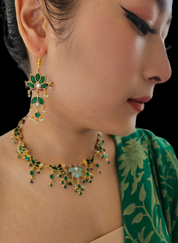 A person wearing a green kundan fish necklace with a turquoise flower element, gold, and green stone details.
