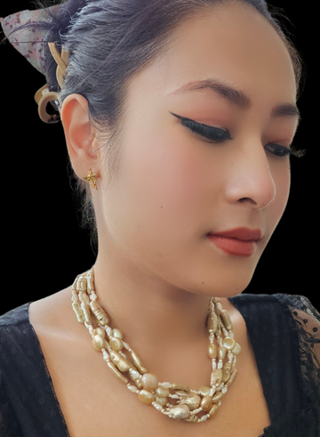 A woman wearing a champagne-colored pearl necklace with white rice pearls, accented with gold-colored beads.