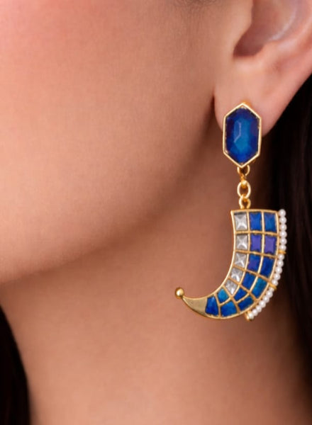 Earring with blue gemstone and gold crescent design worn by a person.