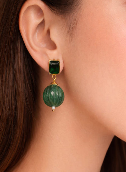 Green gemstone earring with gold setting worn by a person