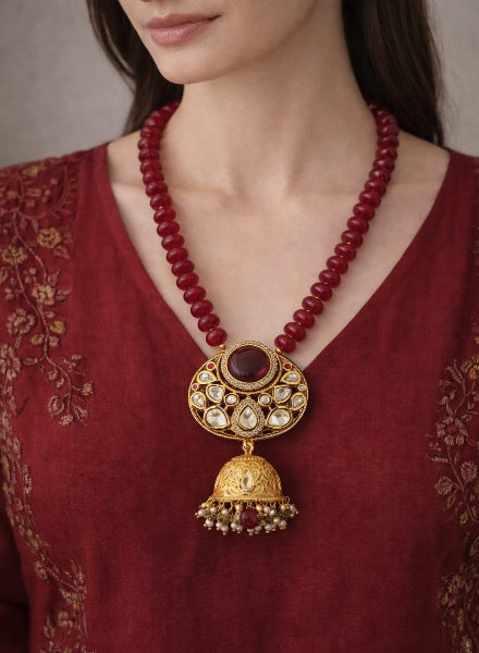 Woman wearing a red beaded necklace with a gold pendant 