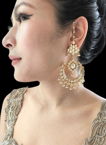 A woman wearing a golden Kundan Chandbali earring set with intricate floral patterns.