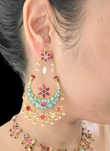 A close-up image of a woman's ear wearing a gold, blue, and red stone chandbali earring.