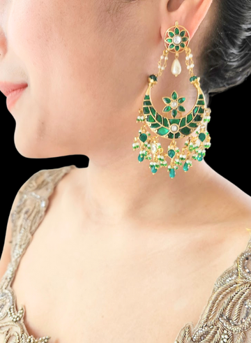 A close-up of a woman's ear wearing a green and gold-colored Kundan Chandbali earring.