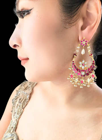A woman wearing a pair of red kundan chandbali earrings with intricate gold and pink detailing.