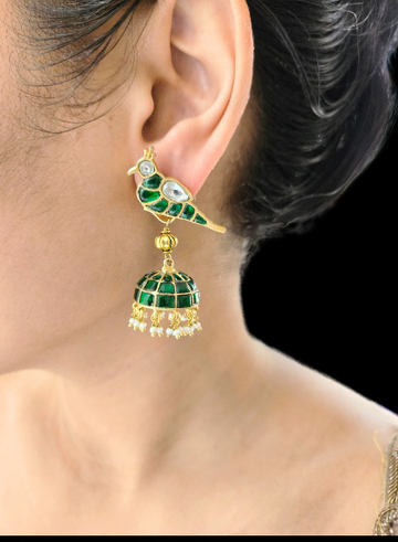 A close-up image of a woman's ear wearing a green and gold-colored kundan-style jhumki earring.