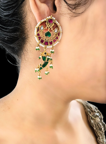 A person wearing a pair of round ruby, green onyx, and pearl earrings with a jade and gold fish drop design.