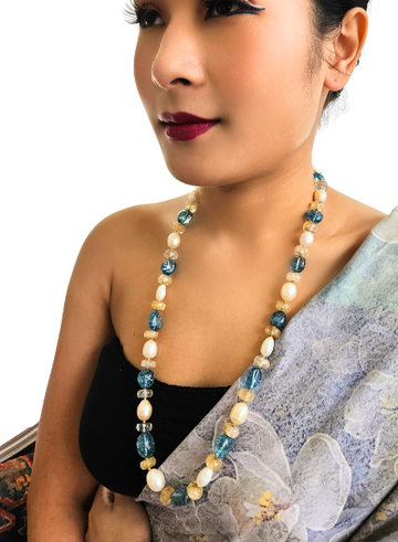A person wearing a black sari and a pearl necklace with blue sapphire accents.