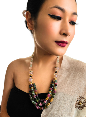 A person wearing a black top and a beige saree, showcasing a multicolored tourmaline and rose quartz multi string necklace with kundan embellishments.
