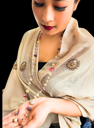 A person holding a long, silver-colored necklace with Harkimer diamonds and raw ruby accents.