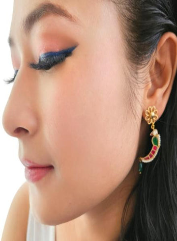 A person wearing a pair of delicate gold-colored bird earrings with kundan-style embellishments.