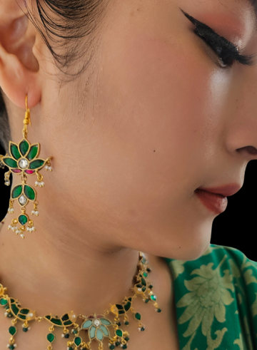 A close-up image of a woman wearing green flower earrings with white pearl accents.