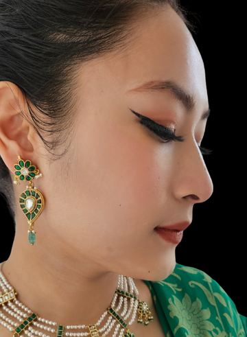 A person wearing a green and gold necklace with a pair of green drop kundan earrings.
