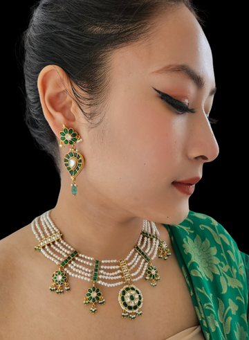 A woman wearing a green and gold traditional attire, adorned with a multi-strand pearl necklace featuring green kundan spacers and floral elements.